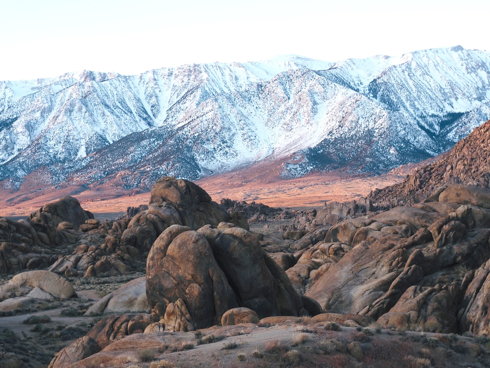 Snow-capped Sierra Nevada peaks rising above the boulders of Alabama Hills at first light